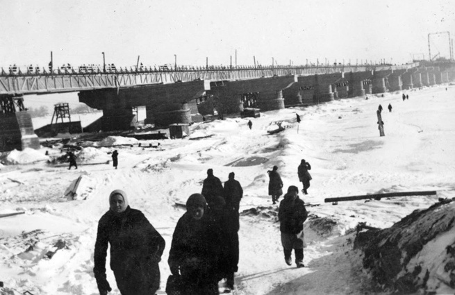Киевляне бредут по замерзшему Днепру вдоль временного достроенного немцами моста фон Рейхенау (бывший Наводницкий мост, строительство которого к началу оккупации не было завершено, и немцы использовали его опоры), зима 1941-1942 года. Во время боев за Киев, осенью 1943-го, мост был взорван